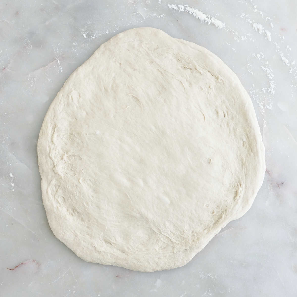 Pizza dough shaped into a circle on a floured counter.