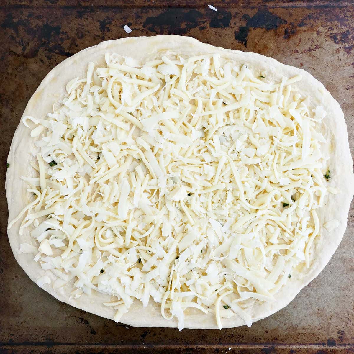 Pizza dough topped with mozzarella and fontina cheeses on a baking sheet.