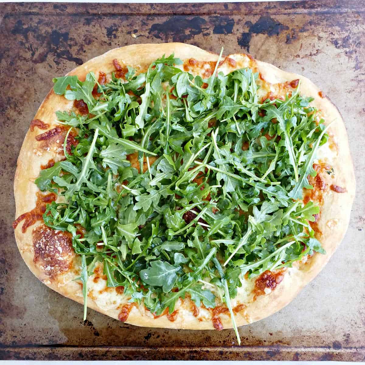 White pizza topped with arugula on a baking sheet before serving.