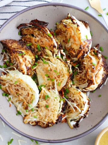 Roasted savoy cabbage wedges in a bowl surrounded by ingredients and napkin.