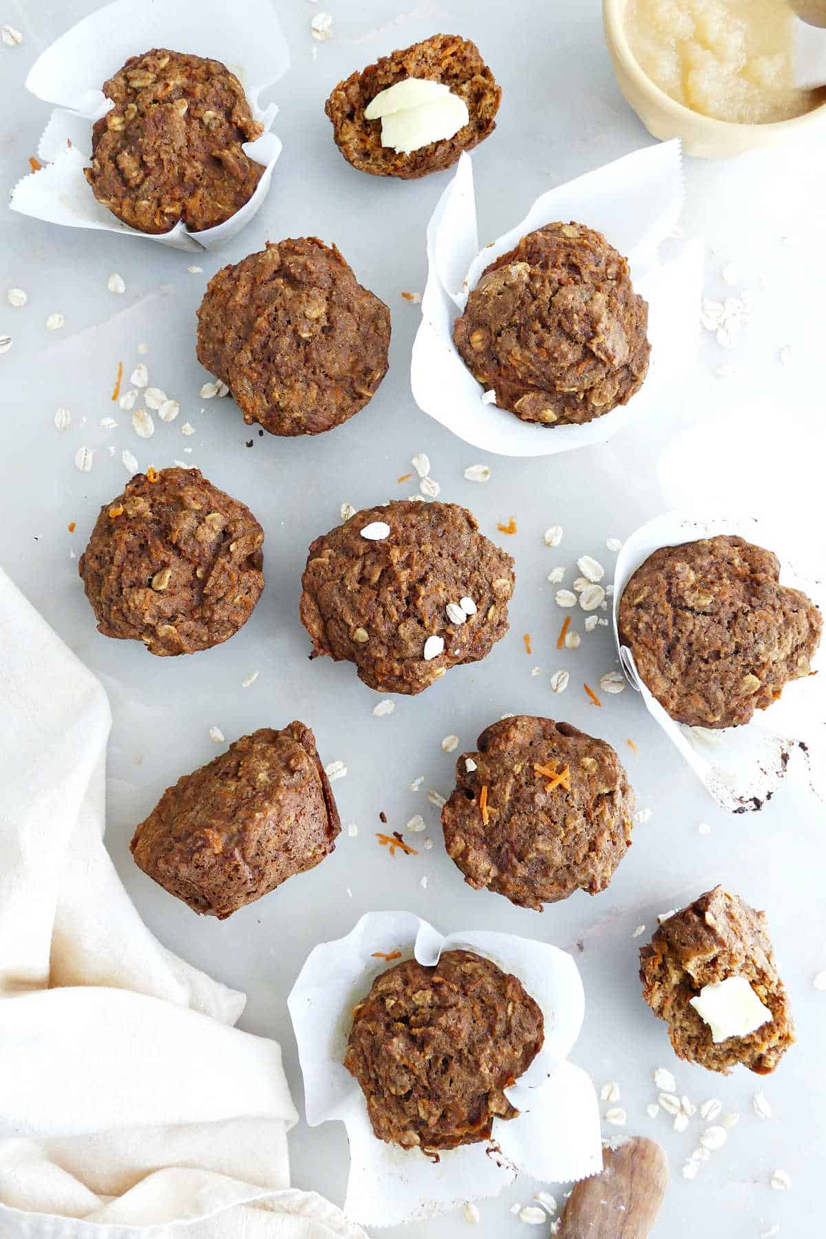 Applesauce muffins on a counter next to a napkin, knife, and ingredients.
