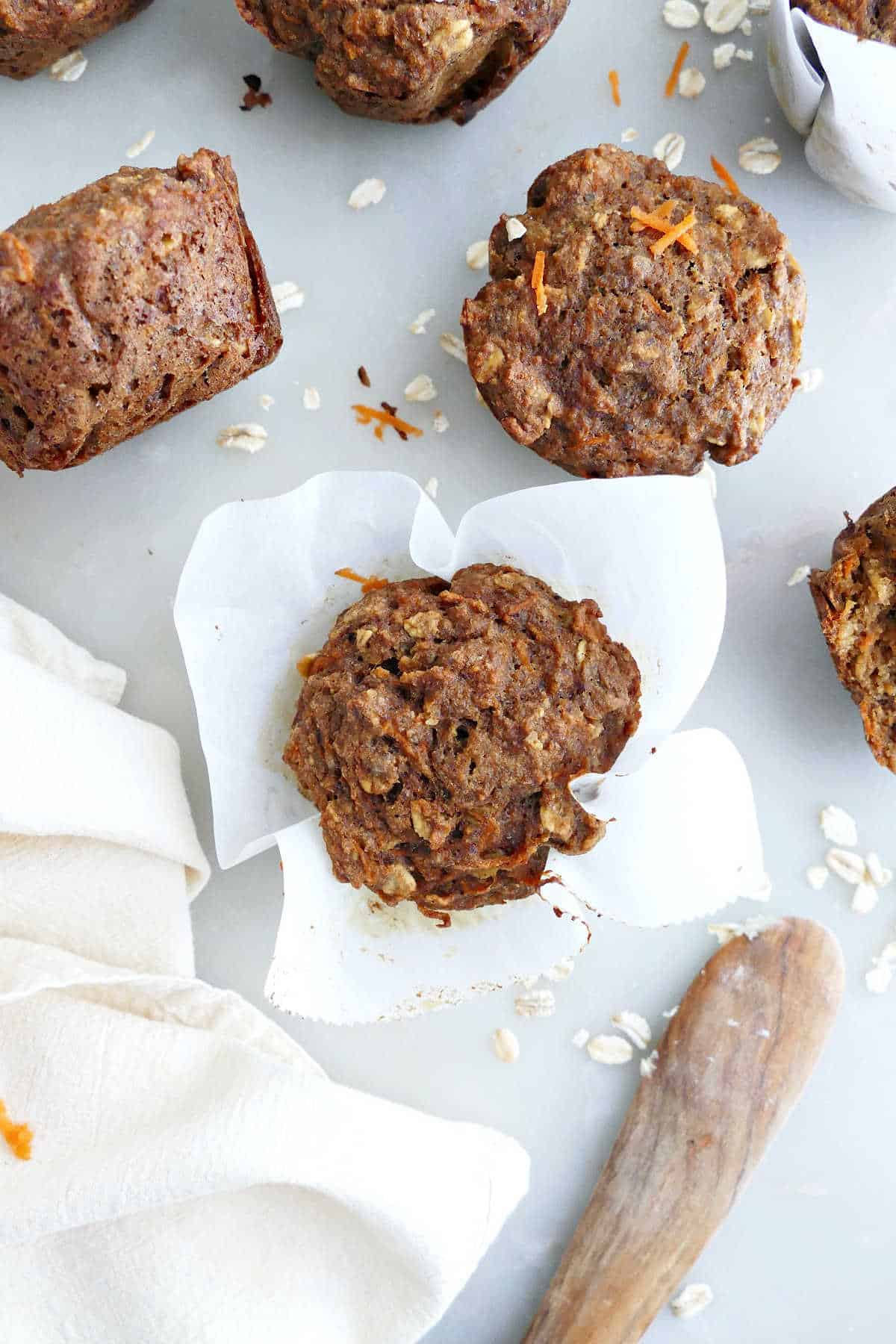 Applesauce carrot muffin in parchment paper next to muffins, napkin, and knife.