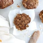Applesauce carrot muffin in parchment paper next to muffins, napkin, and knife.