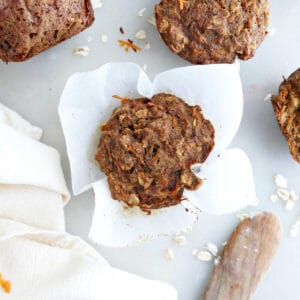 Applesauce carrot muffin in parchment paper next to muffins, napkin, and knife.