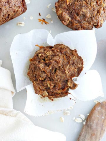 Applesauce carrot muffin in parchment paper next to muffins, napkin, and knife.