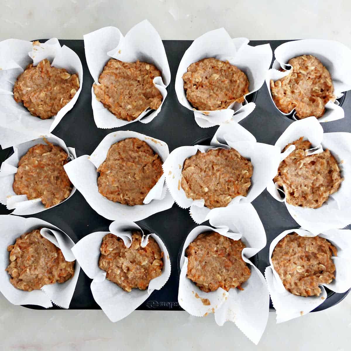 Applesauce muffin batter spooned into a muffin tray lined with parchment before baking.