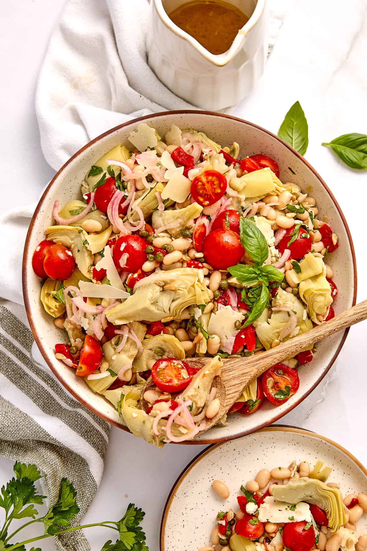 Artichoke salad in a bowl with a spoon next to dressing, napkin, and ingredients.