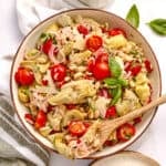 Artichoke salad in a bowl with a spoon next to dressing, napkin, and ingredients.