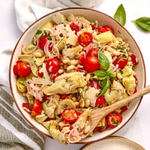 Artichoke salad in a bowl with a spoon next to dressing, napkin, and ingredients.