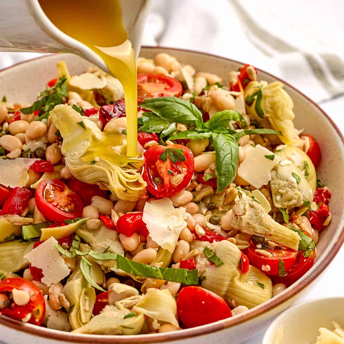 Woman pouring dressing onto artichoke salad in a bowl.