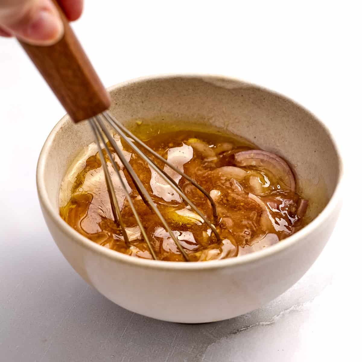 Woman whisking ingredients for red wine vinaigrette in a bowl.