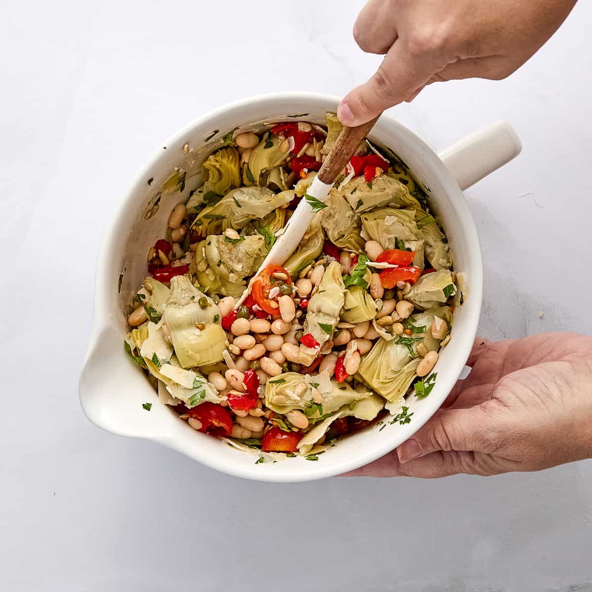 Woman stirring artichoke salad in dressing in a bowl.