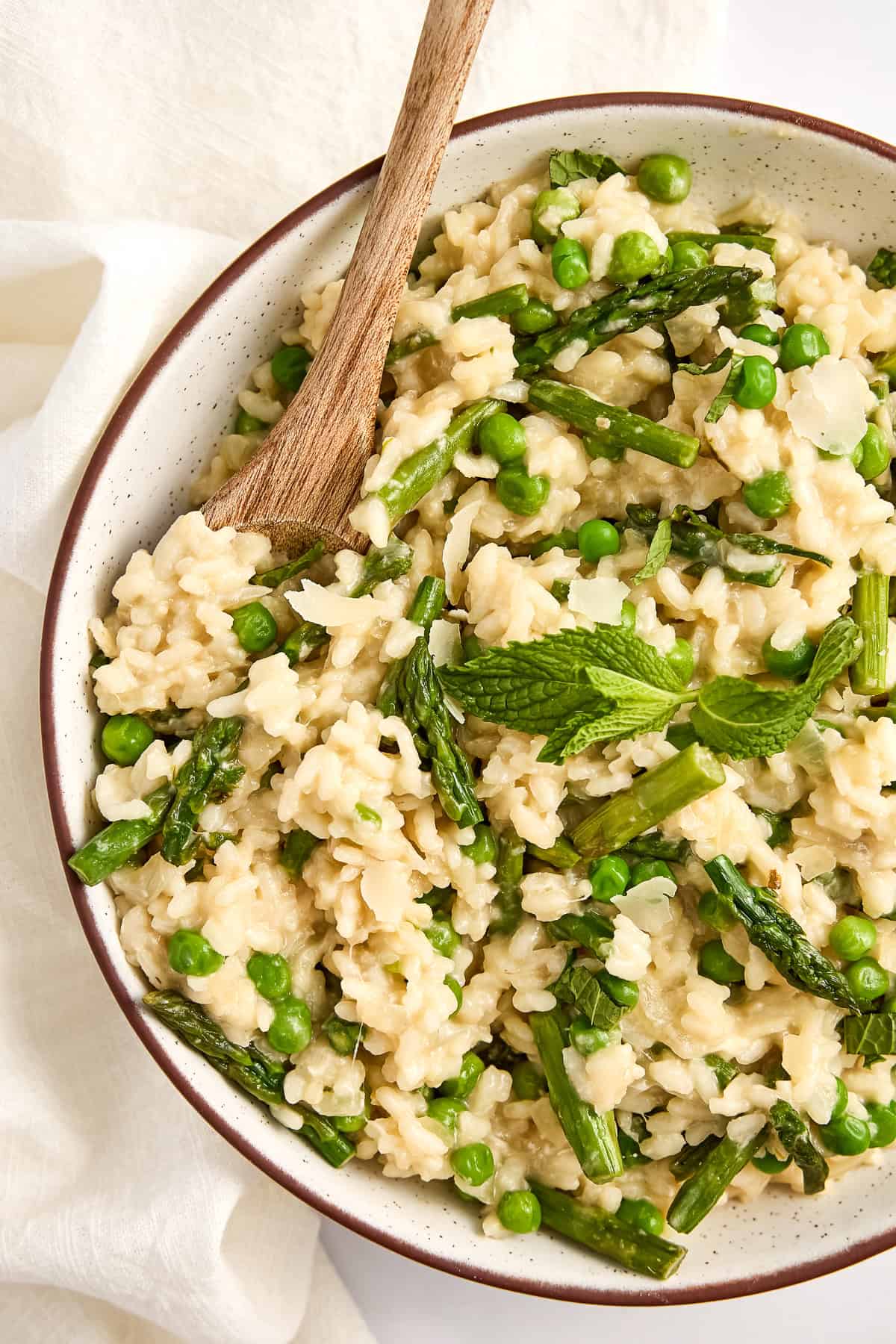 Asparagus and pea risotto topped with mint in a bowl with a spoon.