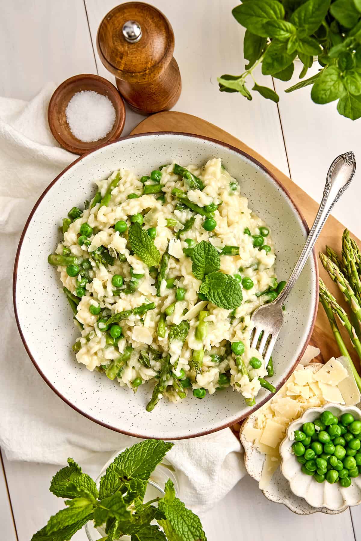 Creamy asparagus and pea risotto in a bowl with a fork on a wooden board.