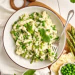 Creamy asparagus and pea risotto in a bowl with a fork on a wooden board.