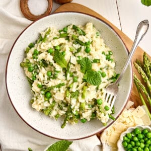 Creamy asparagus and pea risotto in a bowl with a fork on a wooden board.
