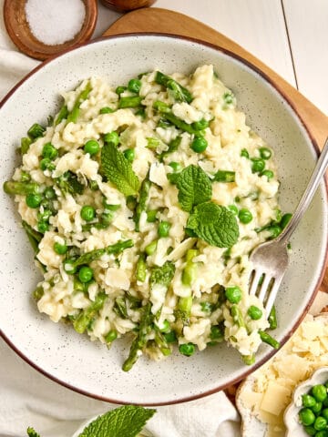 Creamy asparagus and pea risotto in a bowl with a fork on a wooden board.