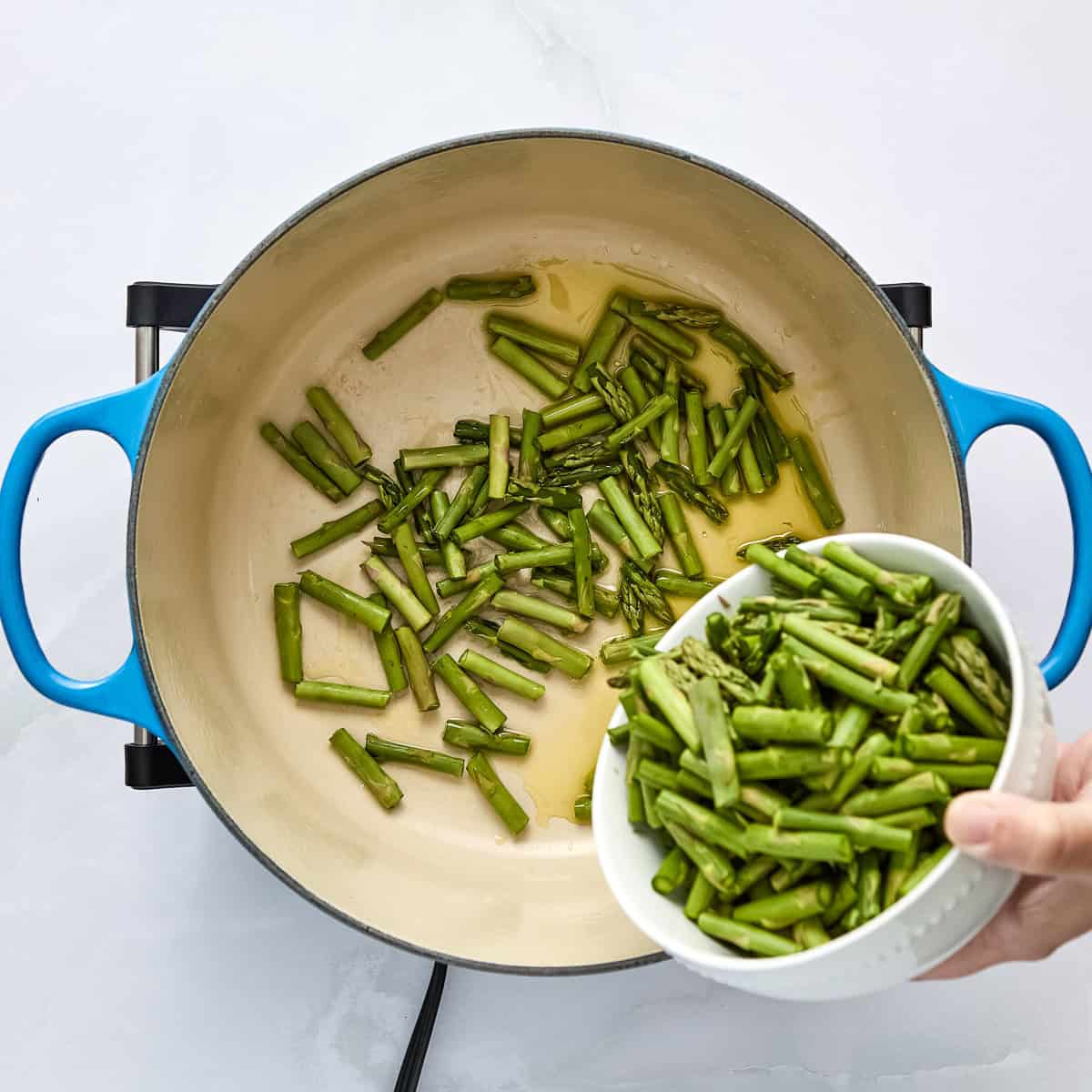 Asparagus pieces being added to a pot with olive oil.