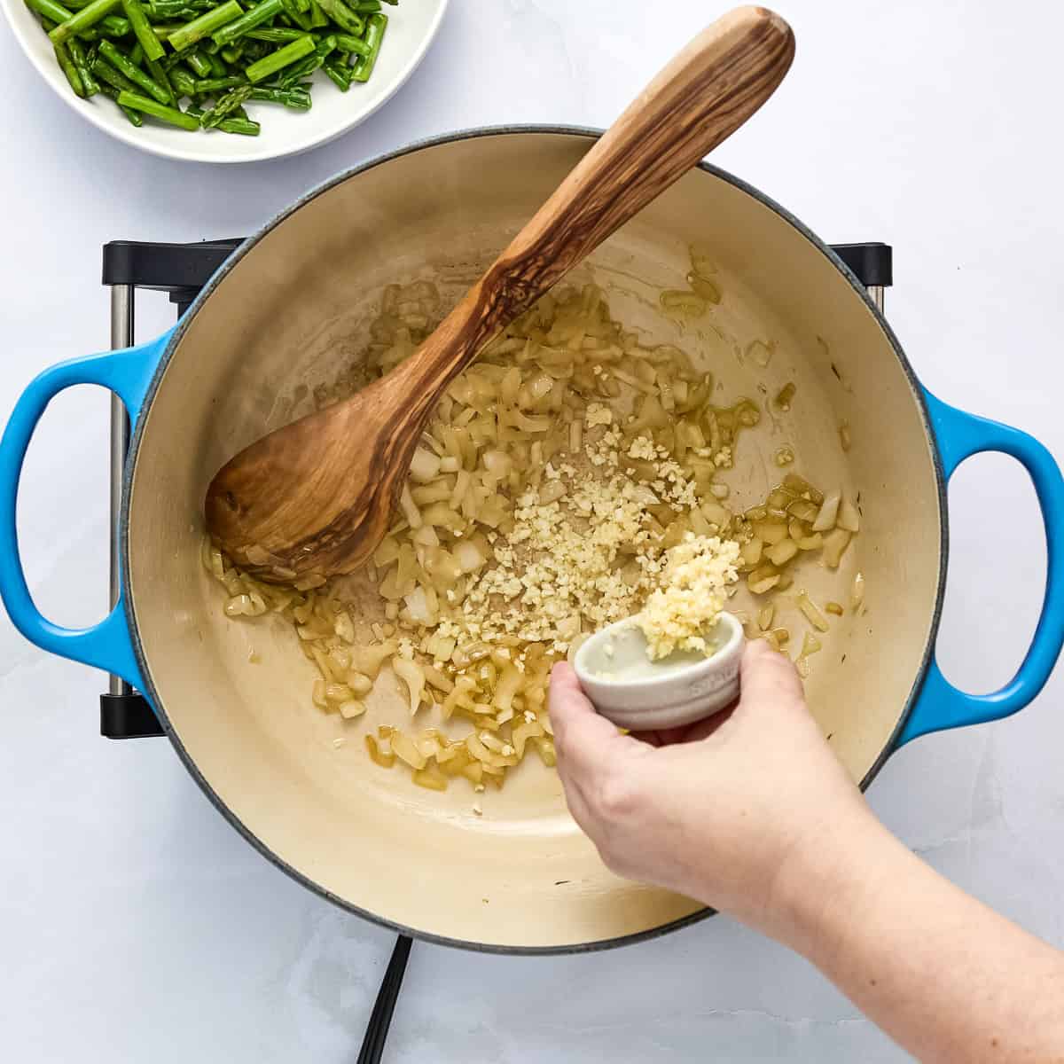Garlic being added to a pot with onion cooking in olive oil.