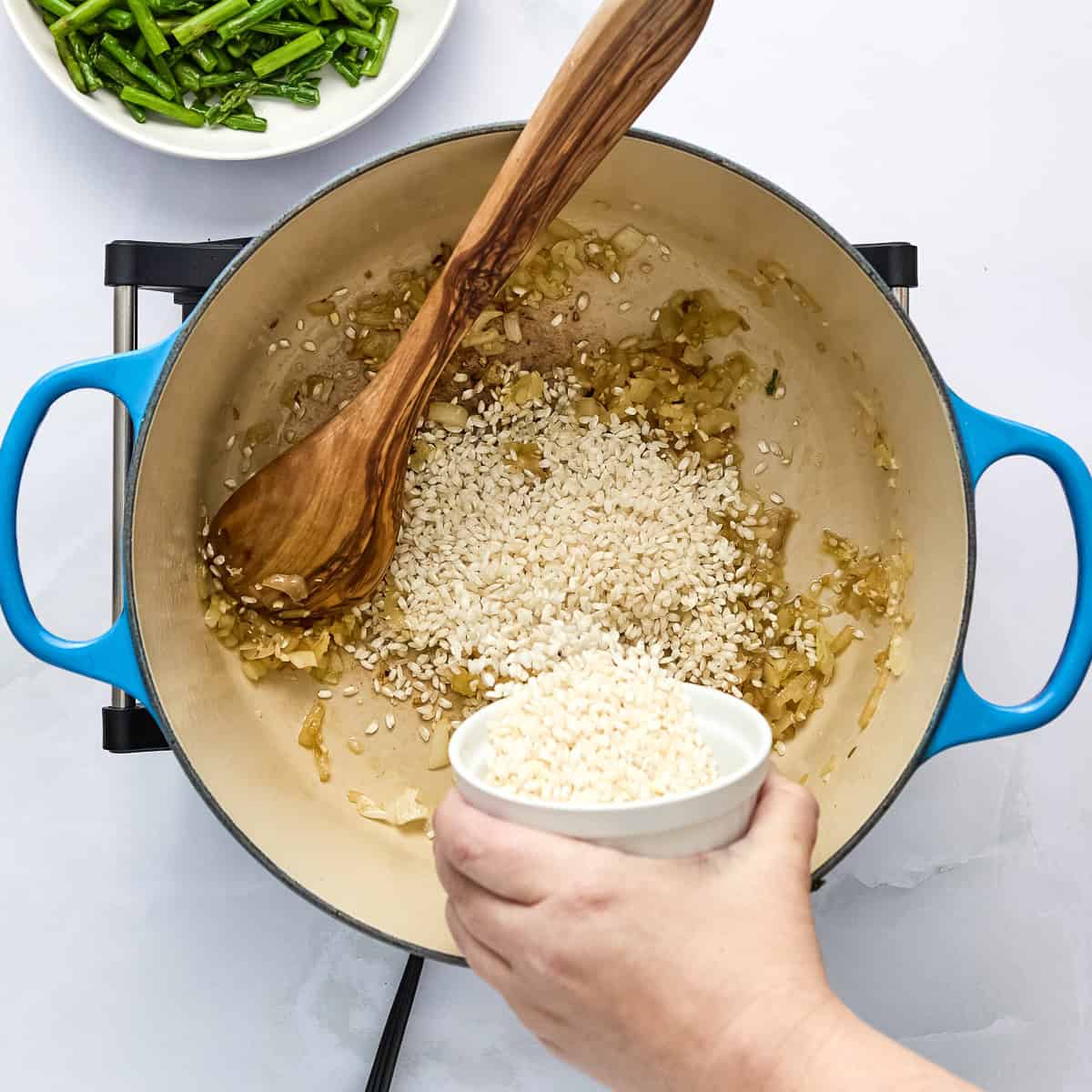 Arborio rice being added to a pot with onion and garlic.