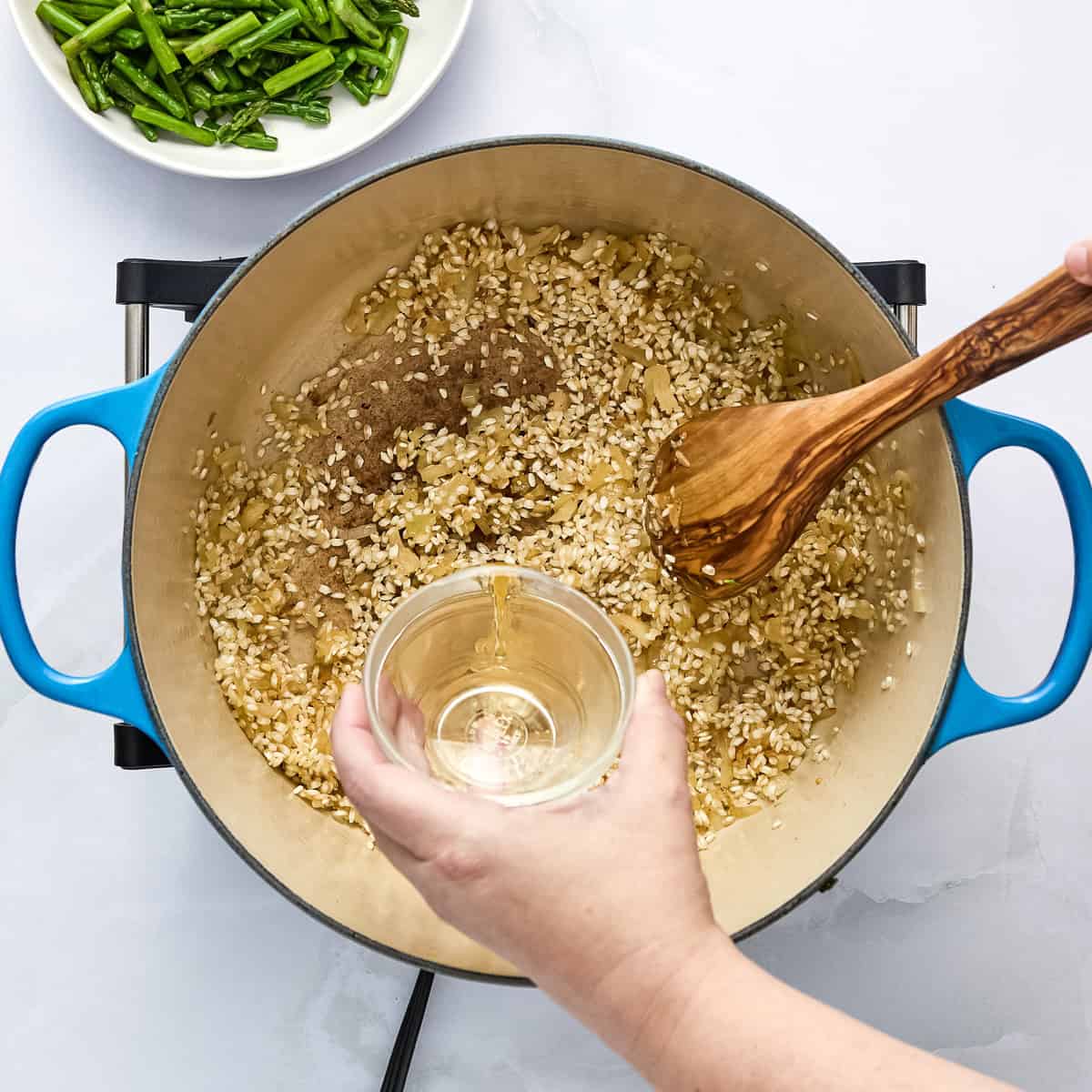 White wine being added to risotto rice in a pot.