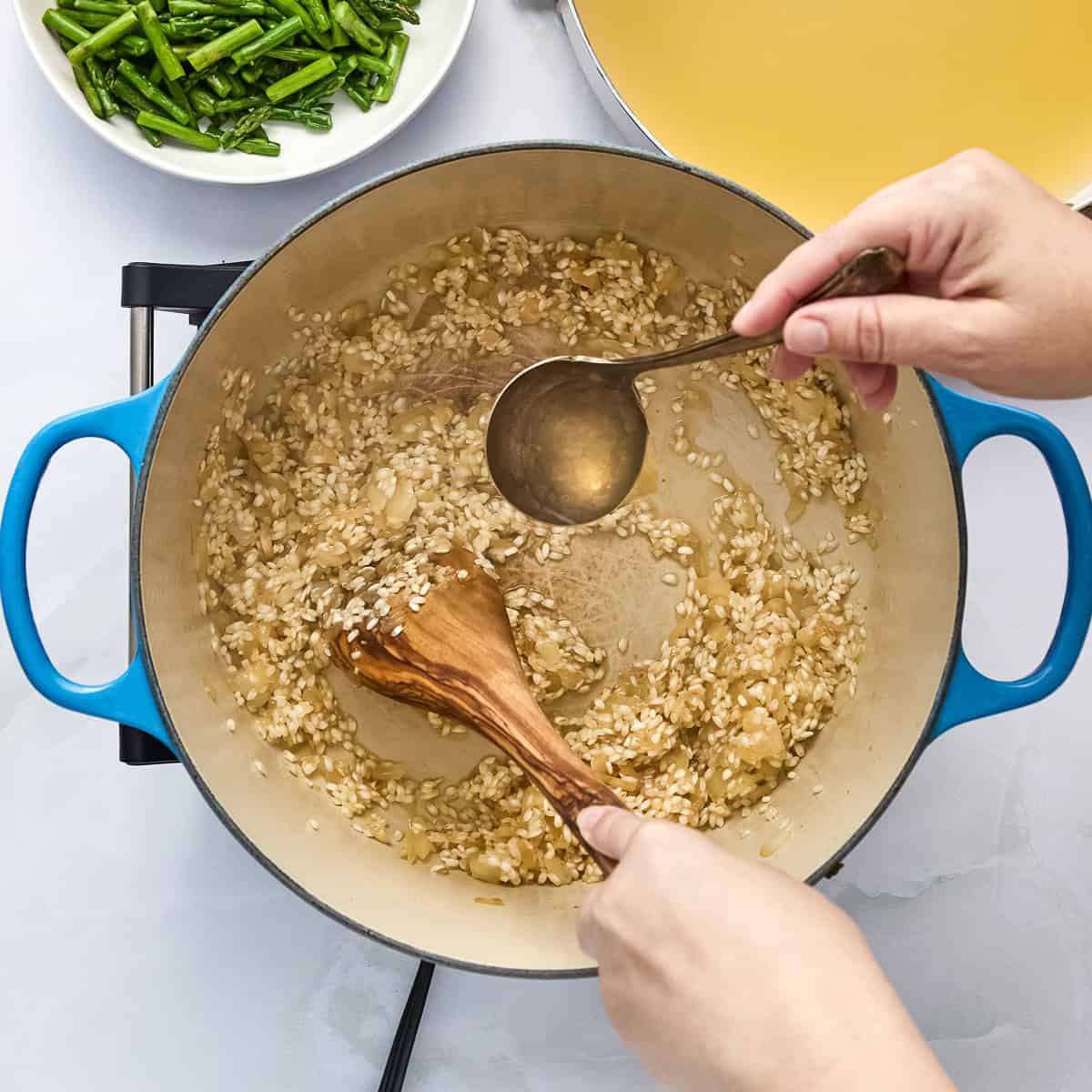 Broth being ladled into a pot with rice for risotto.