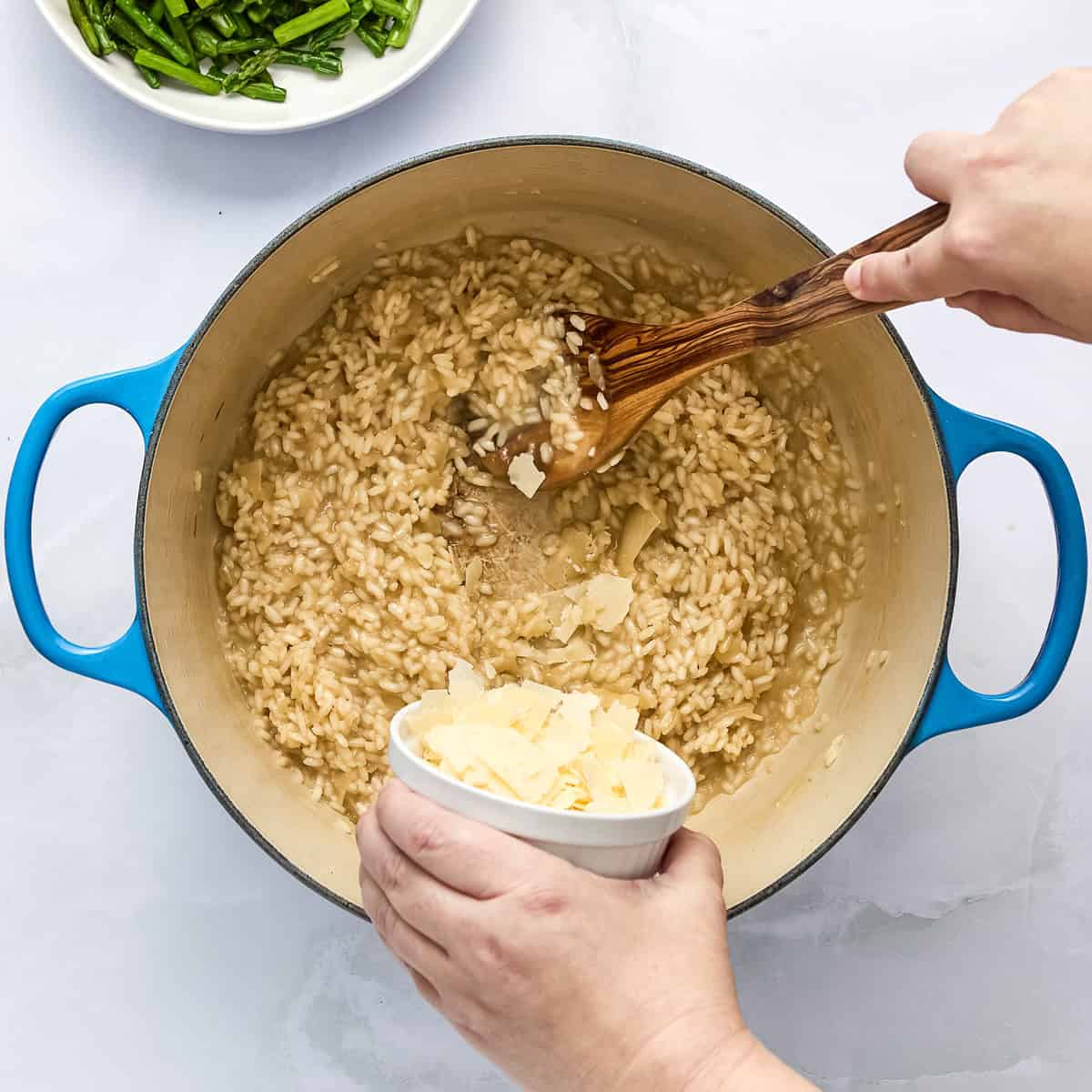 Parmesan cheese being added to a pot with risotto cooking.