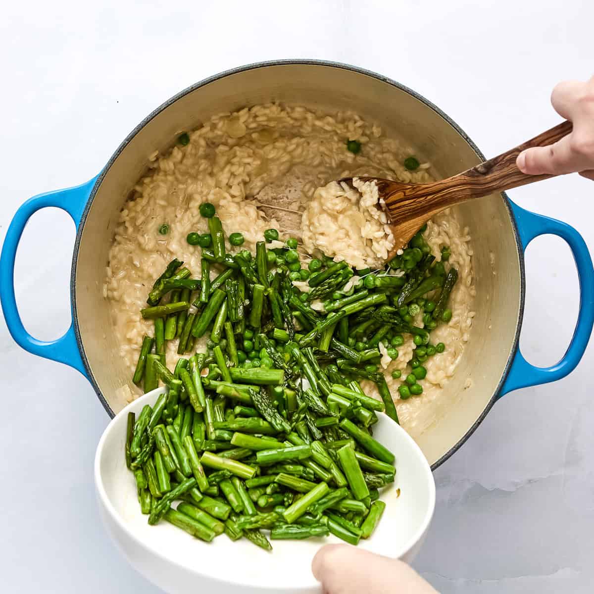 Asparagus and peas being added to risotto in a pot.