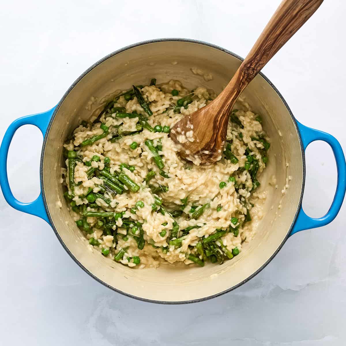 Finished asparagus and pea risotto in a pot with a wooden spoon.