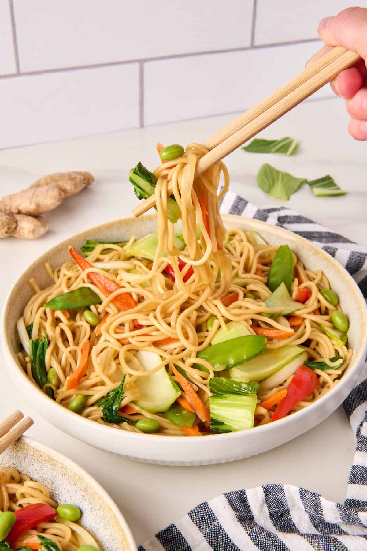 Woman picking up bok choy stir fry and noodles with chopsticks.