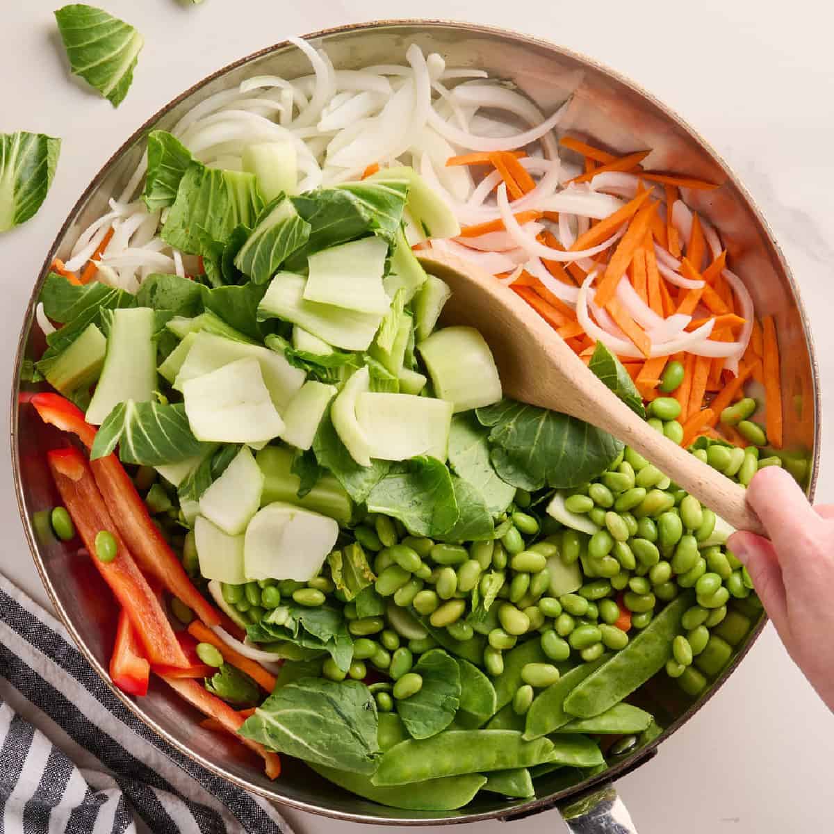 Bok choy and stir fry vegetables in a skillet being stirred with a spoon.