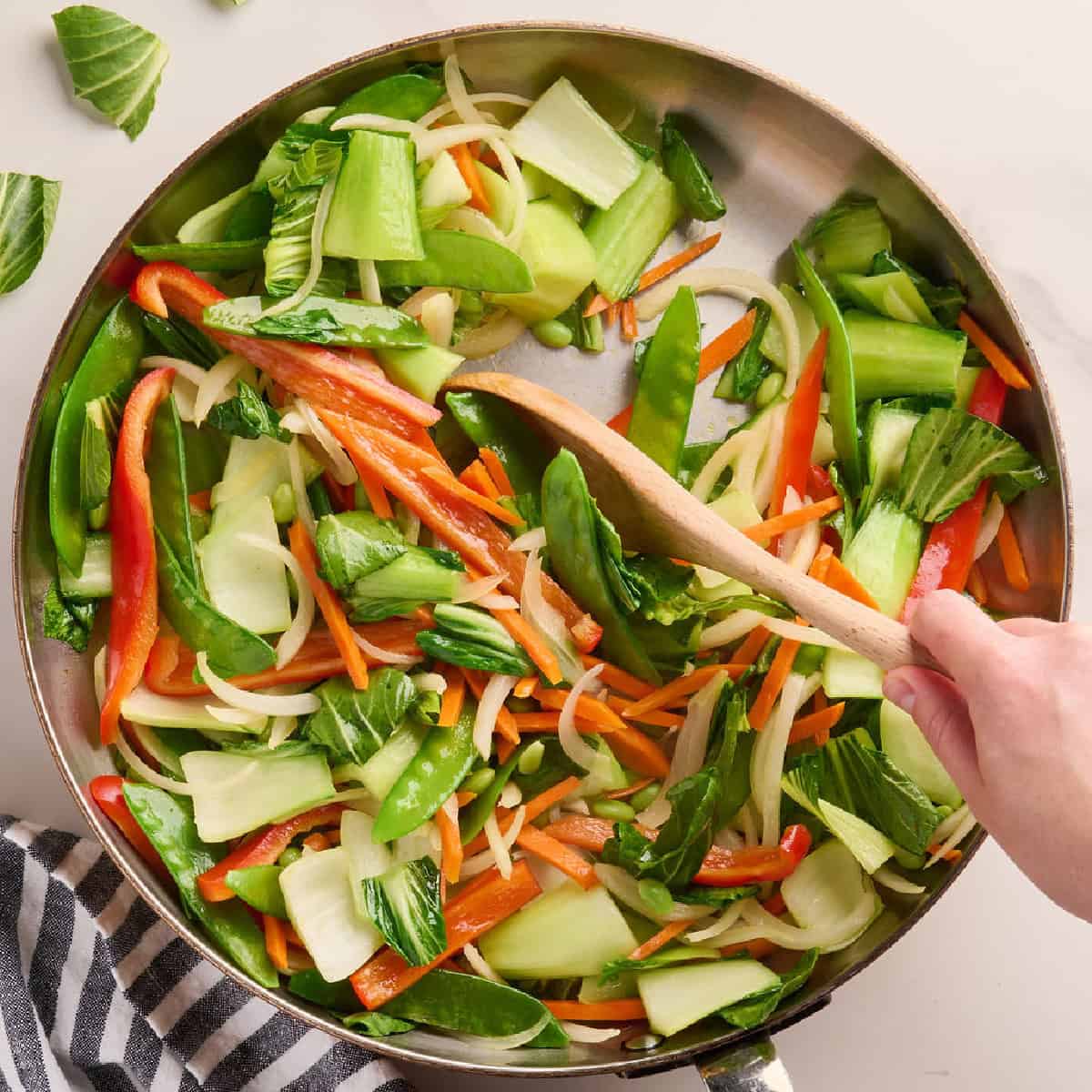 Veggies cooked down in a skillet being stirred with a spoon.