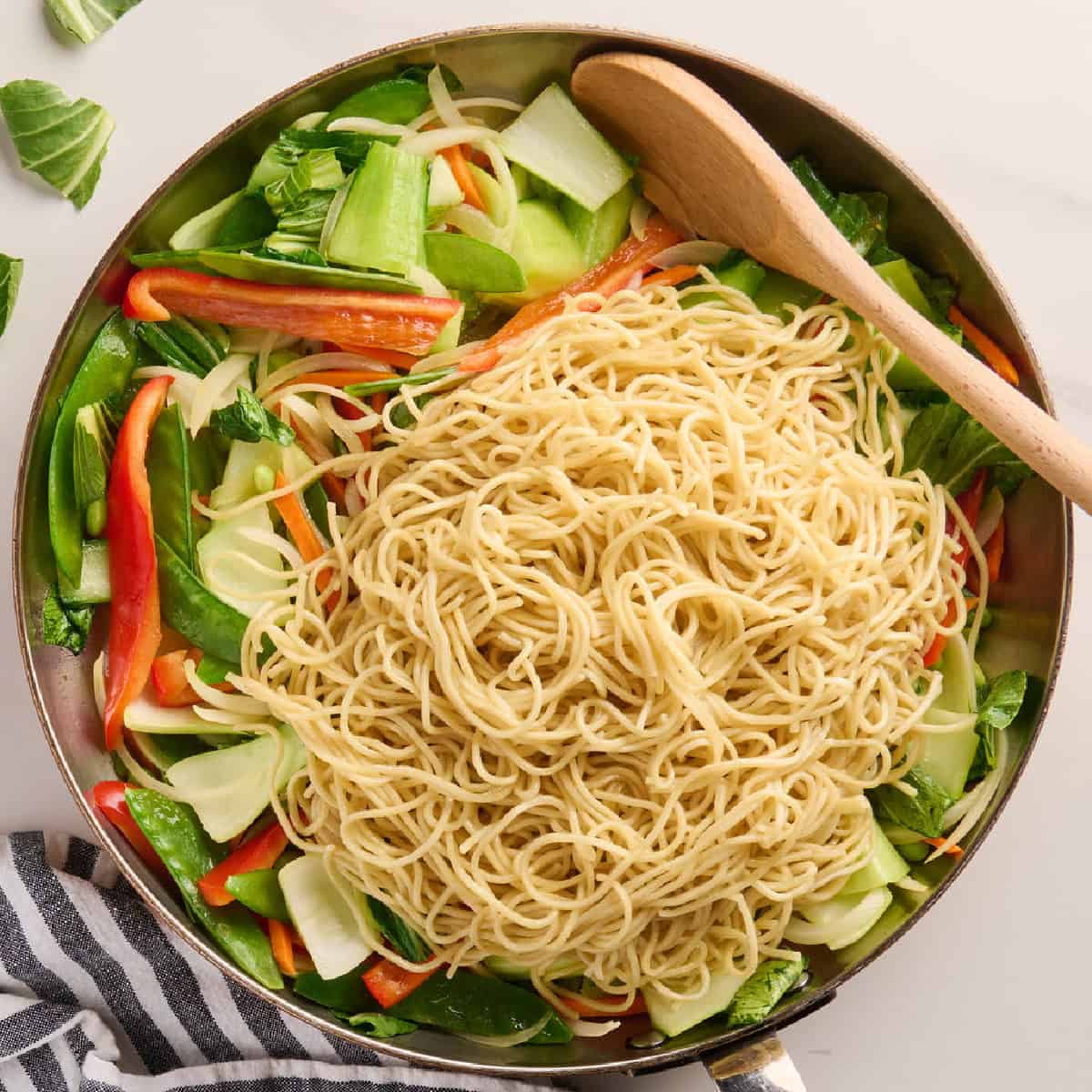 Cooked lo mein noodles added to a skillet of vegetables and bok choy.