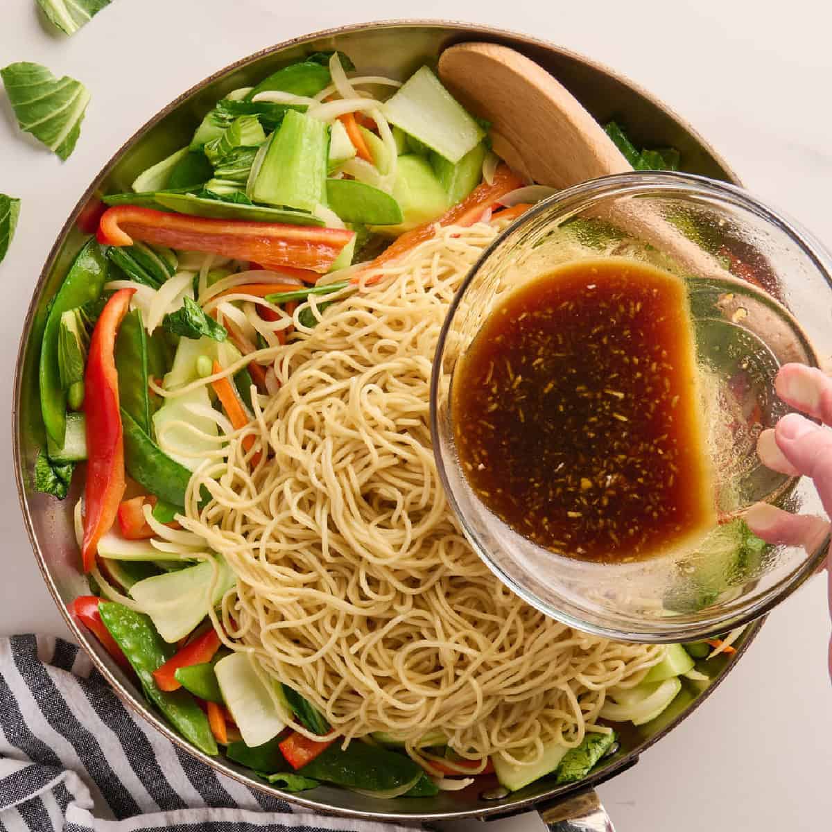 Stir fry sauce being poured over vegetables and noodles in a skillet.