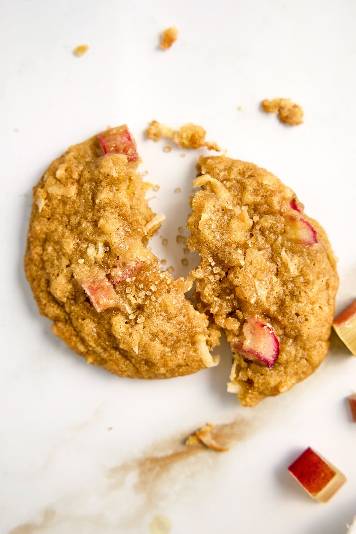 Rhubarb cookie broken in half on a counter next to rhubarb pieces.