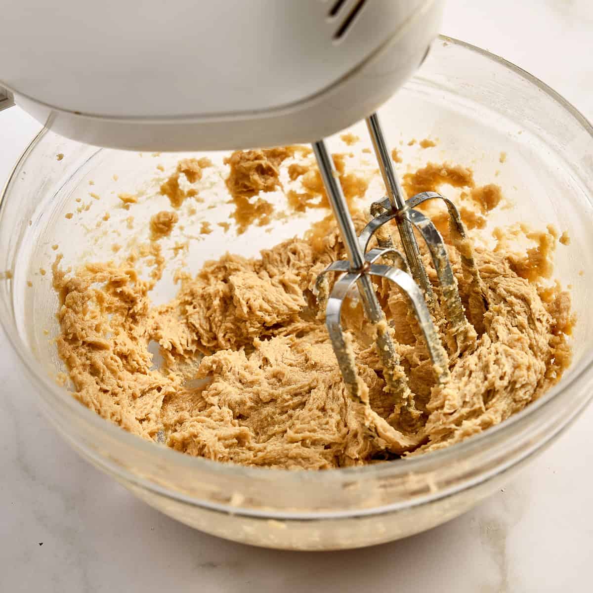 Hand mixer creaming butter and sugar in a mixing bowl.