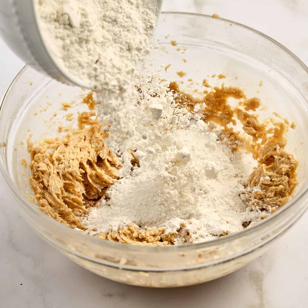 Adding flour to the bowl of creamed butter and sugar.