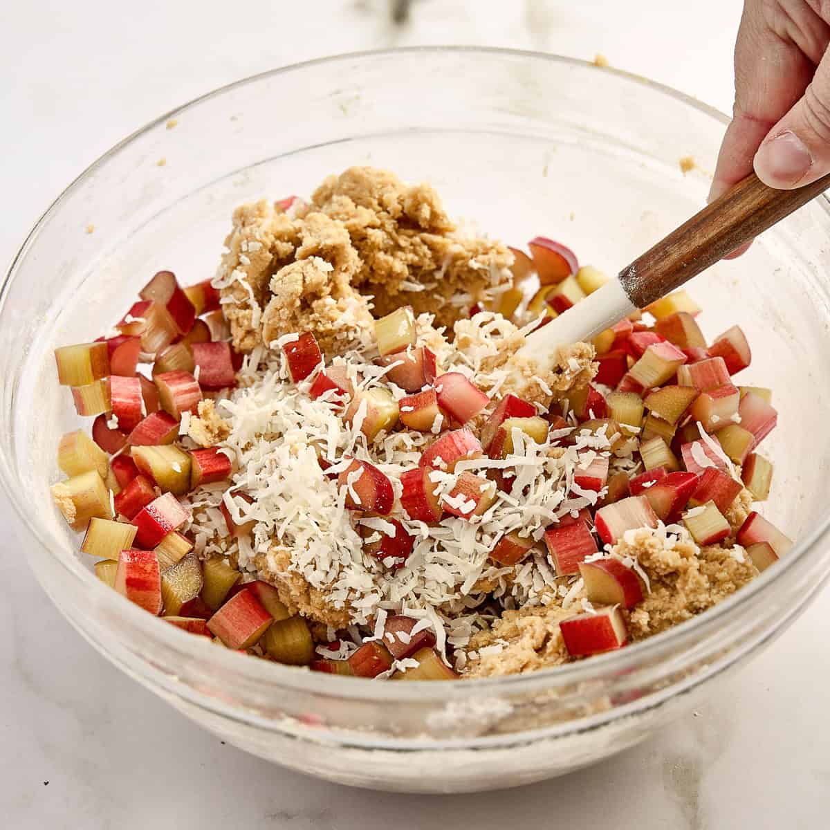 Woman folding rhubarb and coconut into cookie batter with a spatula.
