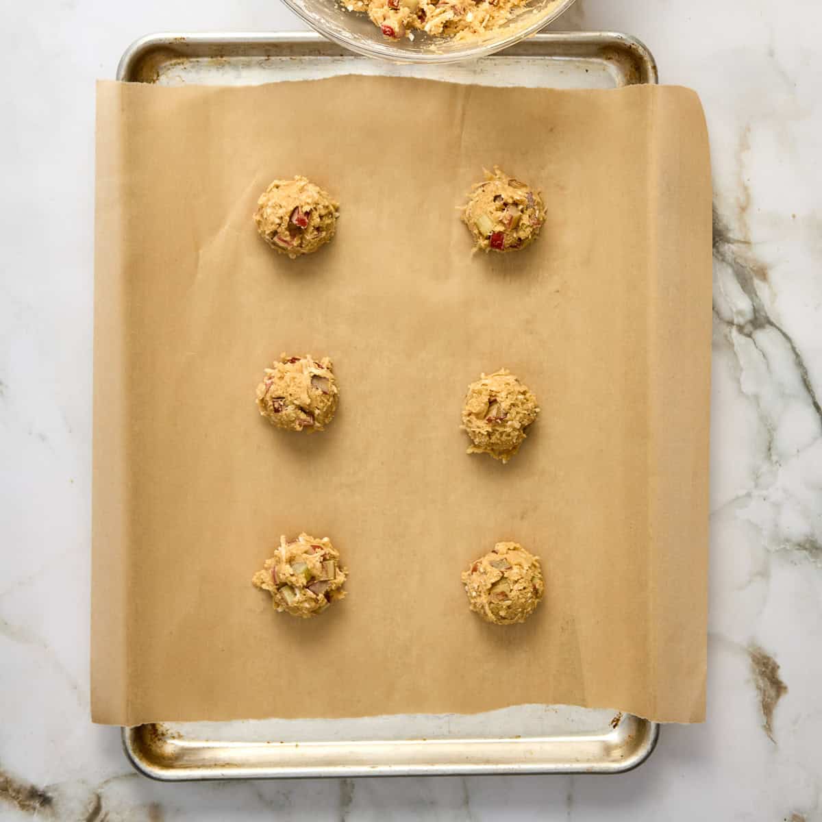 Six cookie dough balls placed on a baking sheet lined with parchment paper.