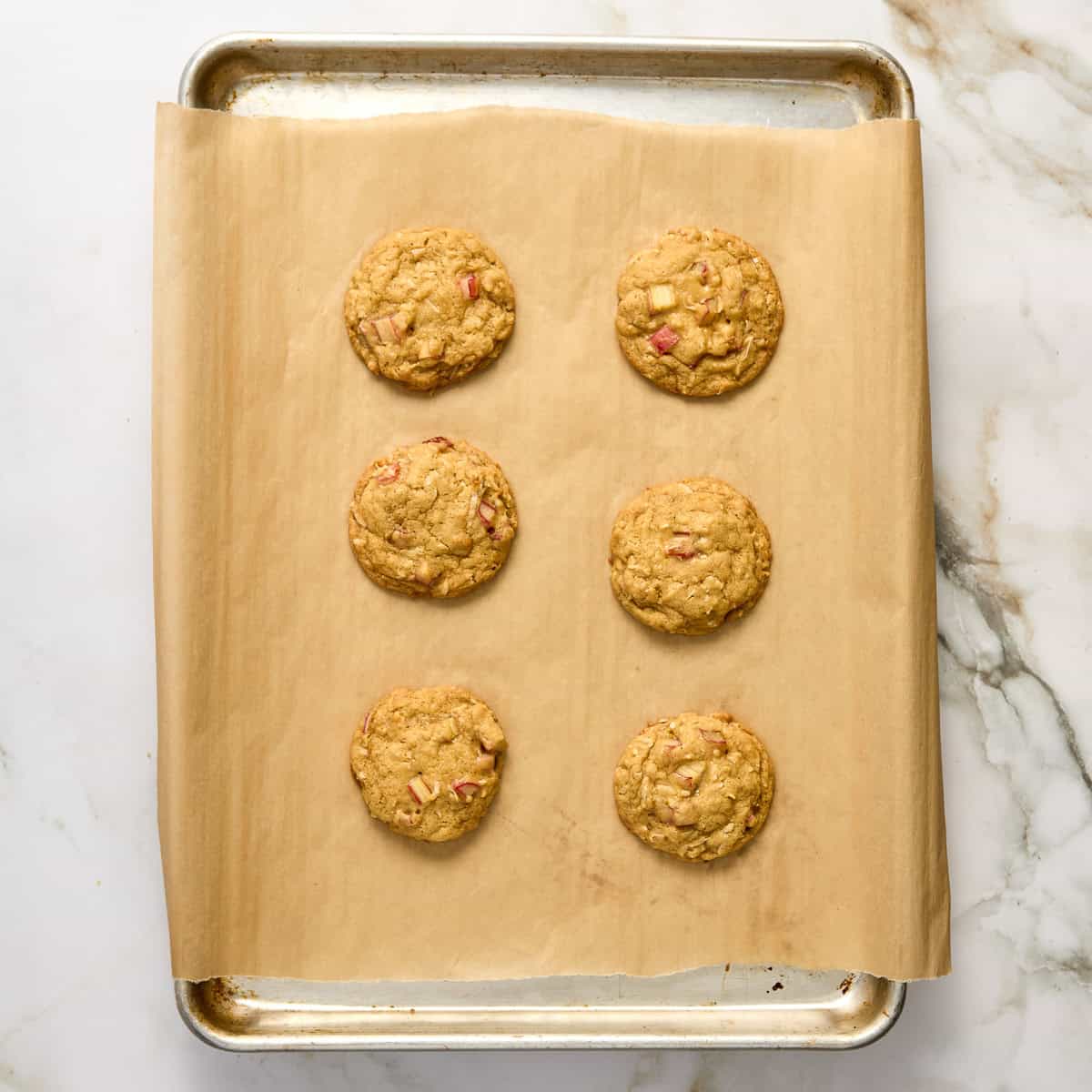 Six rhubarb cookies on a lined baking sheet after coming out of the oven.