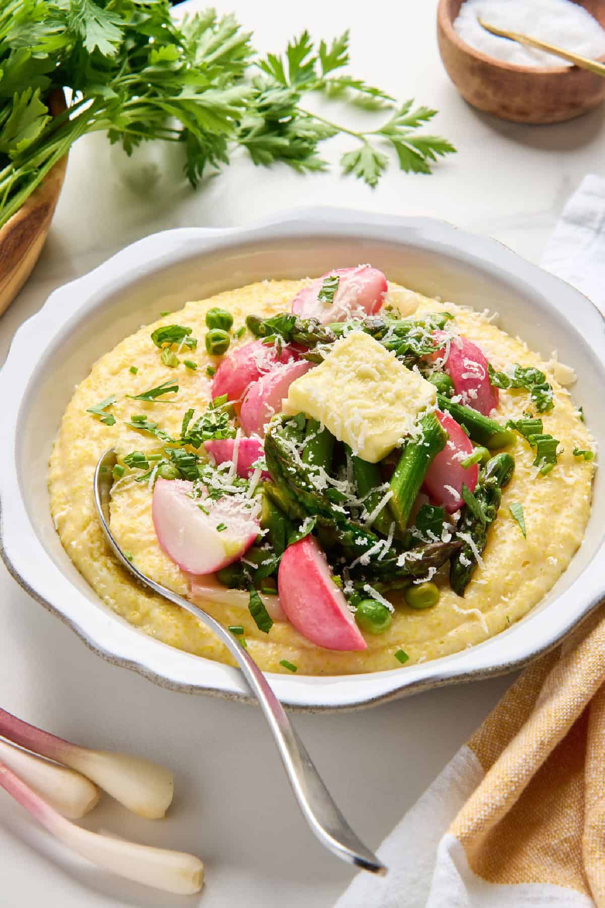 Bowl of spring polenta with vegetables topped with cheese with a spoon in it.