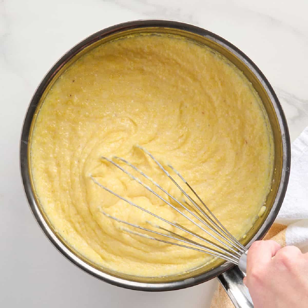 Creamy polenta being whisked in a pot while cooking.