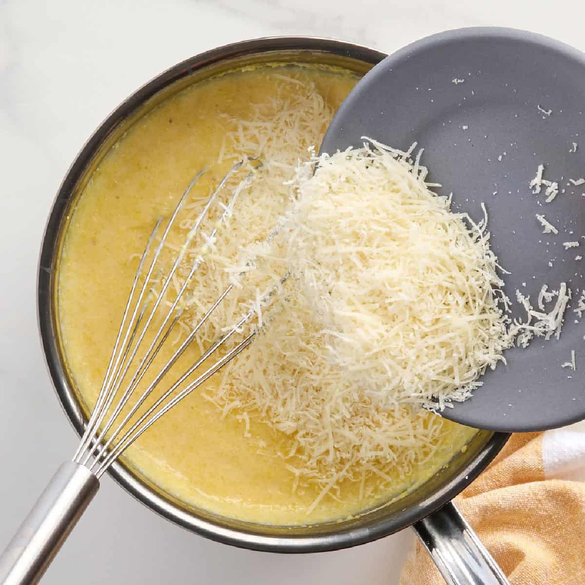 Parmesan cheese being sprinkled into a pot with polenta.