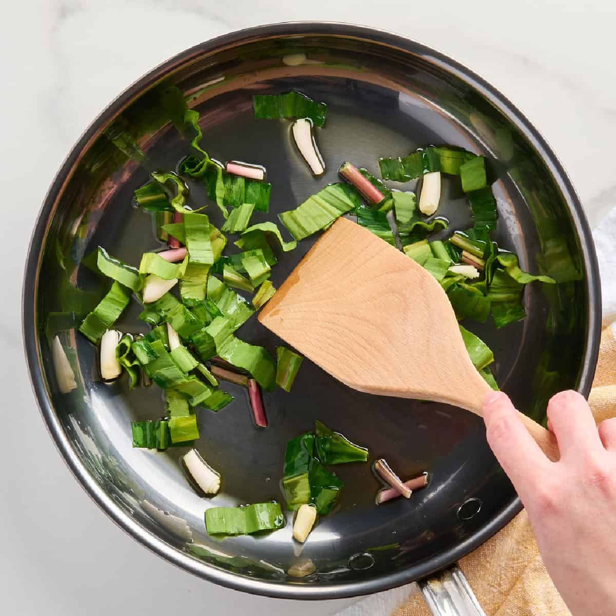 A woman stirring ramps cooking in oil in a skillet.