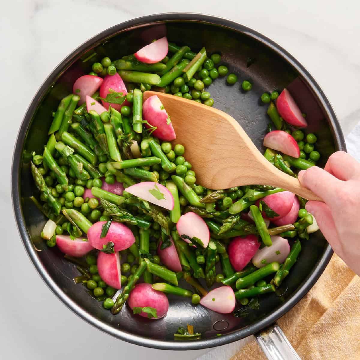 A woman stirring spring vegetables in a skillet to be served over polenta.