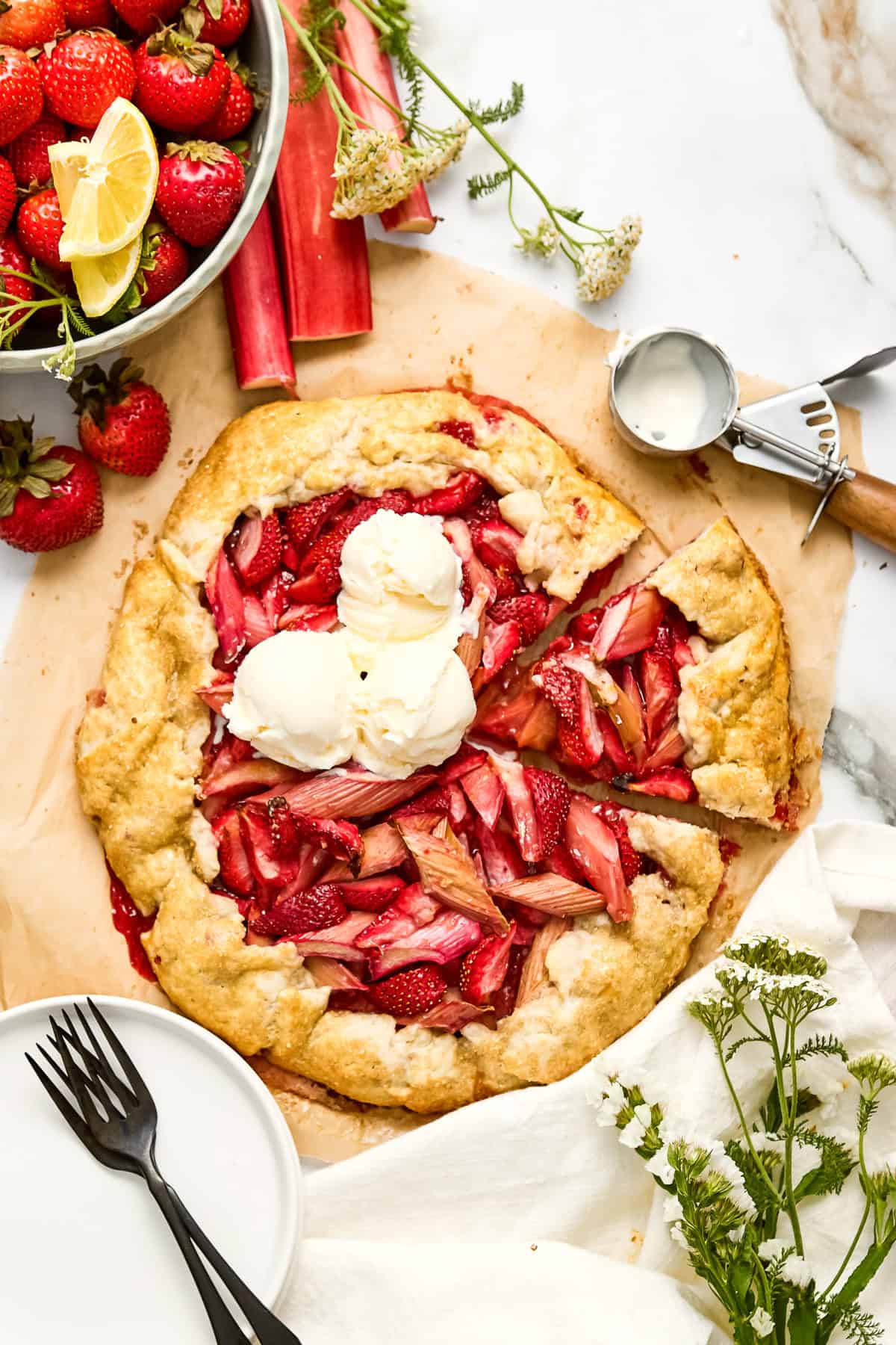 Rhubarb and strawberry galette with scoops of vanilla ice cream on a counter next to ingredients.