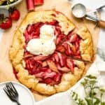 Rhubarb and strawberry galette with scoops of vanilla ice cream on a counter next to ingredients.