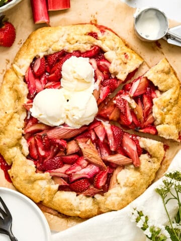 Rhubarb and strawberry galette with scoops of vanilla ice cream on a counter next to ingredients.