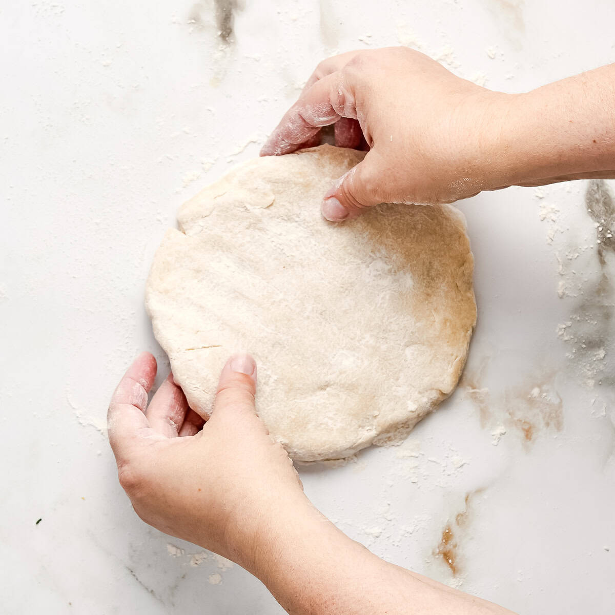 Woman holding a flattened disk of galette dough on a floured surface.