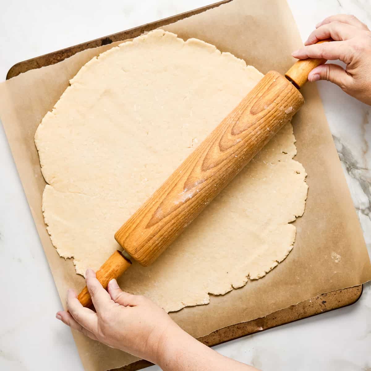 Woman using a rolling pan to roll galette dough into a circle on a baking sheet.